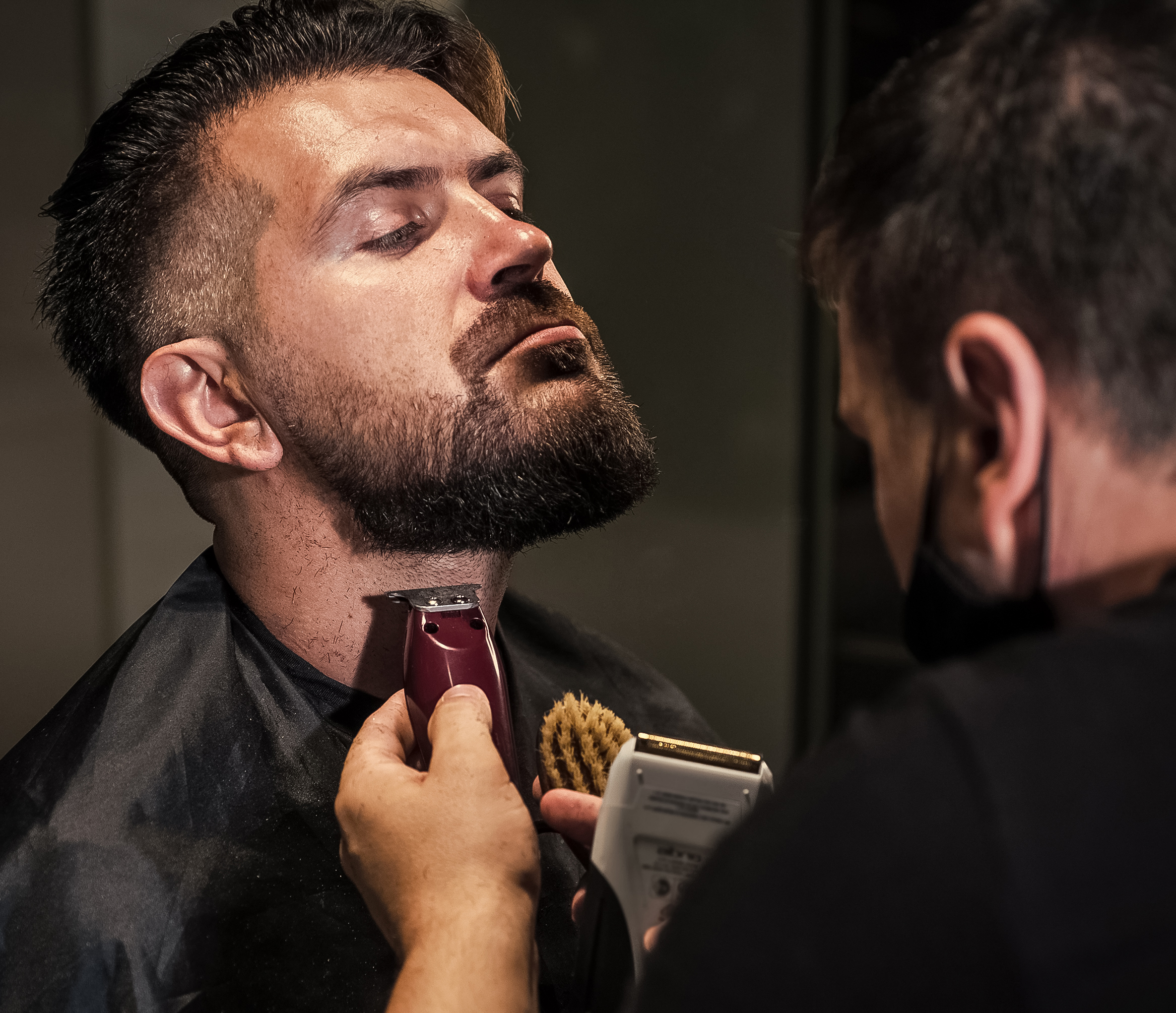 Getting perfect shape of mature bearded man getting beard haircut by hairdresser at barbershop, Designing new hairdo.